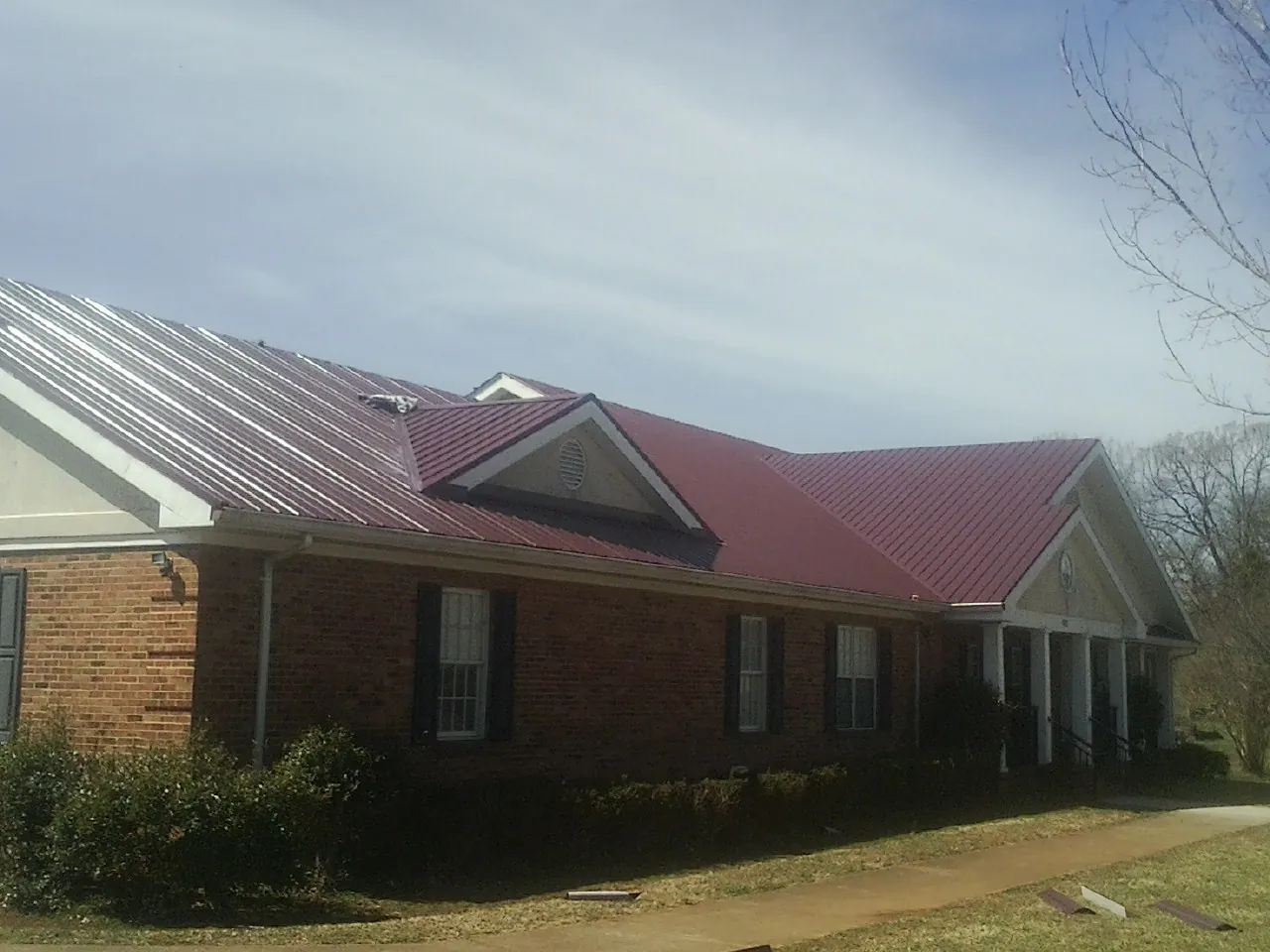Red metal roof with gabled entries on a long brick building, from a Hail Damage Roof Repair job in Lamoure