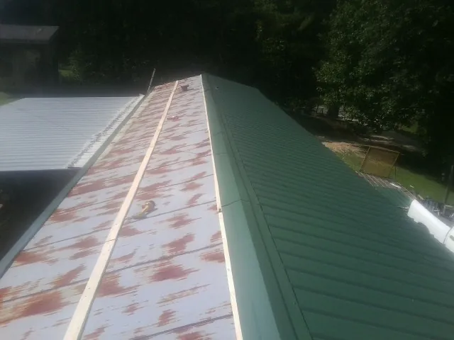 Old rusted panels beside newly installed green metal roofing — Wind Damage Roof Repair by Roofing Brothers in Lamoure