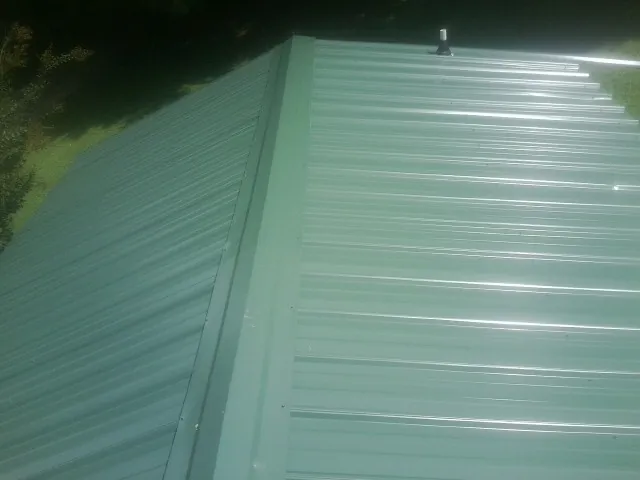 New green metal panels meeting at the ridge of a roof — Flat Roof Repair work by our crew in Lamoure