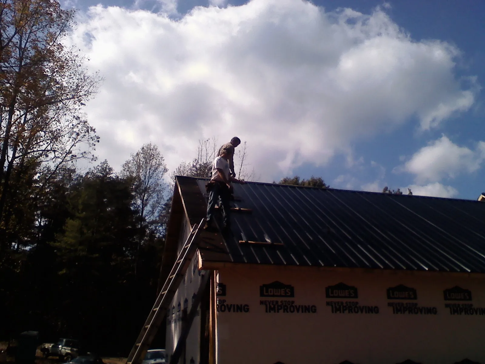 Roofer fastening dark metal panels high against a cloudy sky, from a Roof Inspection job in Lamoure