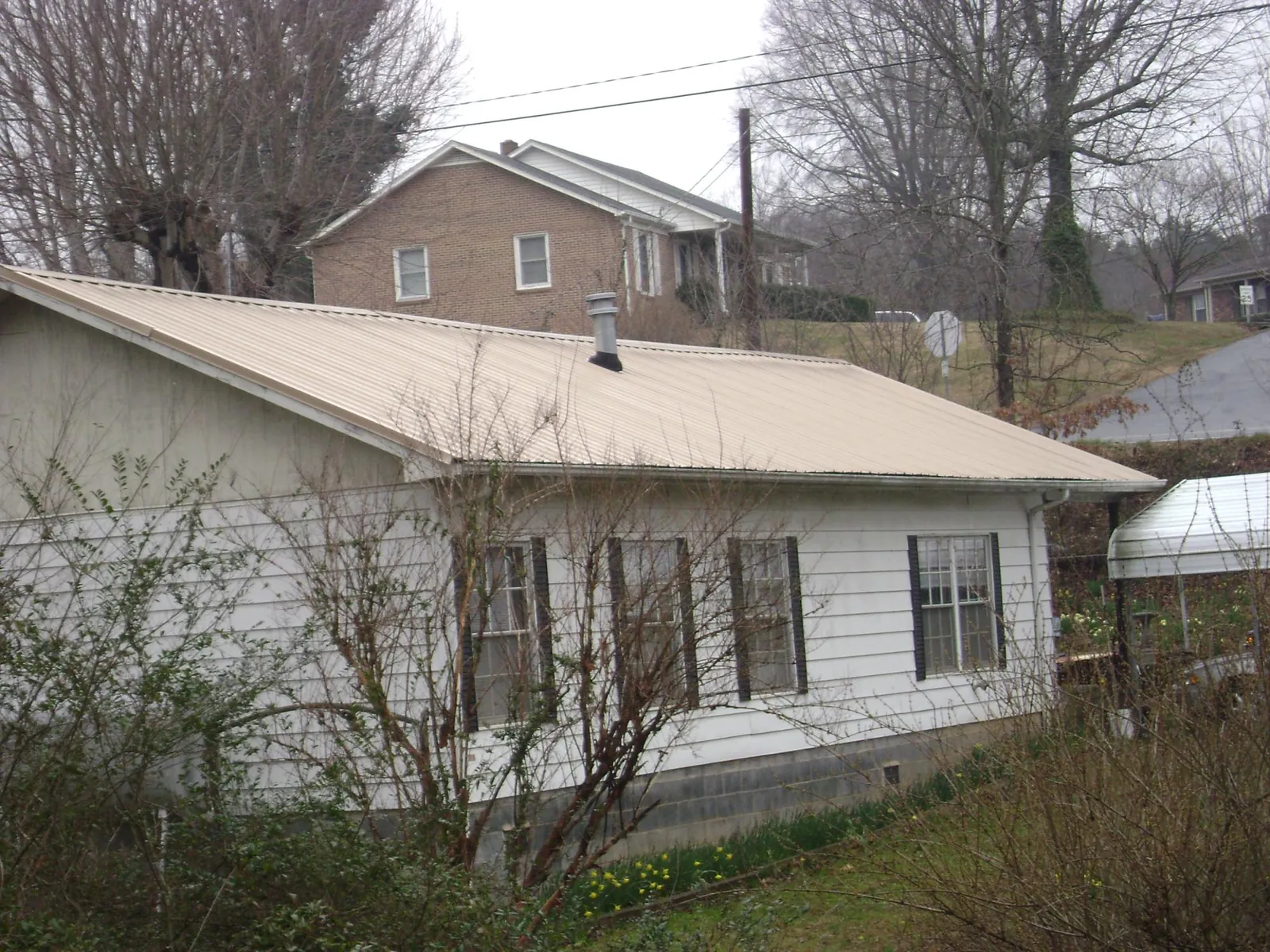 Tan metal roof on a white sided house set into a hillside — Commercial Roofing by Roofing Brothers in Lamoure